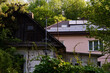 Photovoltaic panels and solar collectors on the roof of the house against the background of green trees; in front of an old crumbling house in the countryside