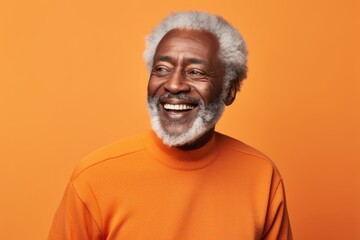 Portrait of a grinning afro-american man in his 80s wearing a thermal fleece pullover in front of soft orange background