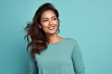 Wall Mural - Portrait of a satisfied indian woman in her 30s sporting a long-sleeved thermal undershirt while standing against soft teal background