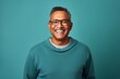 Portrait of a merry indian man in his 50s dressed in a comfy fleece pullover in soft teal background
