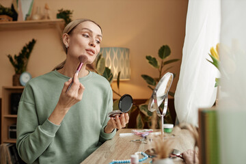 portrait of elegant young woman doing make up looking in mirror by window copy space