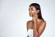© peopleimages.com - Indian woman, skincare and moisturizing lotion in studio for dermatology facial, white background or mockup space. Female person, hand and cream application on face or sunscreen, mask or treatment