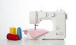Modern automatic white sewing machine with pink fabric and multi-colored spools of thread on the table. White background. Tailoring and clothing repair services. Copy space for text