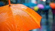 A vivid close-up of a rain-splattered orange umbrella highlights the dreariness of a rainy day with blurred city life behind