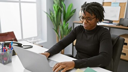 Sticker - Clueless young black woman with dreadlocks, shrugging her shoulders at the office, puzzled face expression while working on laptop, embodying the doubt concept.