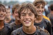 A joyful, muddy young boy smiling widely with his similarly dirty teammates out of focus in the background at a sports event