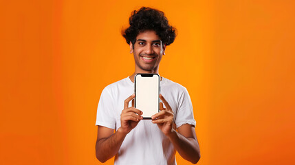 Aufkleber - Positive curlyhaired happy Indian guy in white tshirt holds smartphone with mockup blank white screen stands on isolated orange background looks at camera and smiles friendly : Generative AI
