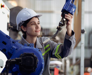 Wall Mural - Industrial engineer woman working on robot arm maintenance in futuristic technology factory. Technician checking robotic automated welding torch machine to control electronic welder innovation process