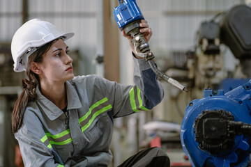 Wall Mural - Industrial engineer woman working on robot arm maintenance in futuristic technology factory. Technician checking robotic automated welding torch machine to control electronic welder innovation process