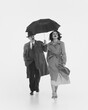 © master1305 - Elegant beau young woman in coat walking with man proposing her his umbrella. Relationship. Monochrome image. Concept of retro and vintage, fashion, human emotions, lifestyle