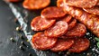 Close up view of a pile of pepperoni next to sliced sausage on a black surface