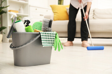 Wall Mural - Woman cleaning floor, focus on different supplies in bucket at home