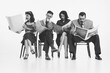 Group of four people, men and women in retro-style clothes sitting on chair and reading newspapers, journals with shocked face on white background. Monochrome image. Concept of retro and vintage, news