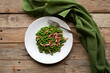 A white plate is filled with vibrant green peas and crispy pieces of bacon, accompanied by a silver fork on the table next to it. A green napkin enhances the rustic atmosphere.