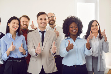 Wall Mural - Group of business people men and women looking at camera, showing thumbs up sign and smiling. Company employees team or a group of staff standing in office. Teamwork and success concept.