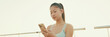 © Andrii Nekrasov - Close-up of smiling asian girl in sports top using cellphone while standing on waterfront on modern buildings background in morning light, Panorama
