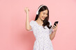 Happy Asian woman using mobile phone and wireless headphone isolated on pink background