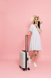 Happy young Asian woman traveler drag luggage isolated on pink background, Tourist girl having cheerful holiday trip concept, Full body composition