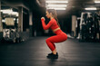 Side view of a fit sportswoman doing squat endurance in a gym.