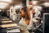 Fototapeta Kwiaty - A strong black sportswoman is doing overhead triceps extension with dumbbell at gym.