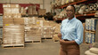 Confident young African woman holding a clipboard in a large warehouse