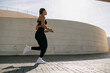 Side view of woman in sportswear is running on modern buildings background. Active lifestyle concept