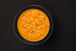 Spicy asian cream soup in black bowl on black background with copy space, top view