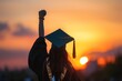 © SKIMP Art - Close up photo of a female student wearing a black graduation cap and gown, raising her arm in the air with a diploma at sunset Generative AI