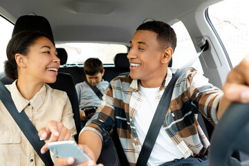 Positive family have car ride, using smartphone and checking map navigation while travelling, mother point at screen, father driving auto, kid sitting on back sit