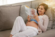 © peopleimages.com - Happy and pregnant woman, reading baby book at home to prepare for motherhood on sofa. Mother, smile and learning to parent with novel or story for education and research to relax before childbirth