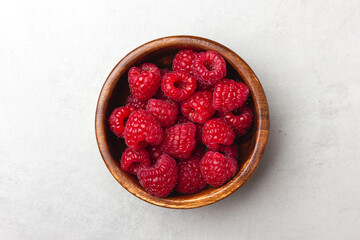 Wall Mural - Raspberries in a wooden bowl on a light grey background