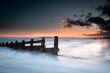 Long exposure landscape photograph at Camber sands beach on a warm evening, Image shows the beautiful sunset and glowing sky with a damaged wooden groyne subject and a receding tide