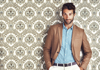 Portrait, confidence and man in suit for fashion on a vintage wallpaper background isolated in studio. Face, style and male person in clothes, blazer and retro pattern of classy model in Switzerland