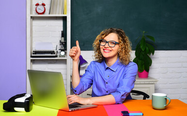 Learning, education and knowledge. Teacher job. University teacher sitting at desk in classroom showing thumb up. Smiling female student in glasses preparing for exam or test in college. High school.