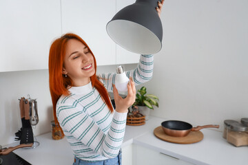 Wall Mural - Pretty young woman changing light bulb in kitchen