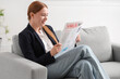 Young businesswoman reading newspaper at home after long working day