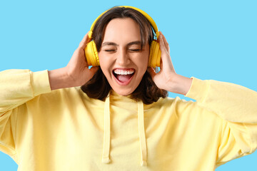 Wall Mural - Young woman in yellow hoodie with headphones on blue background, closeup