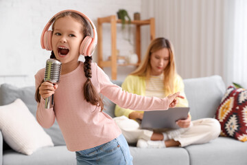 Wall Mural - Noisy little girl in headphones with microphone singing at home