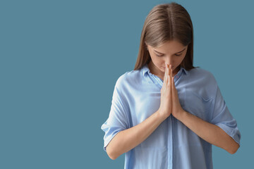 Wall Mural - Young woman praying on blue background