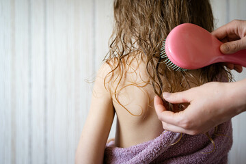 Mom combing her daughter's hair after washing, combing wet hair, baby hair care concept