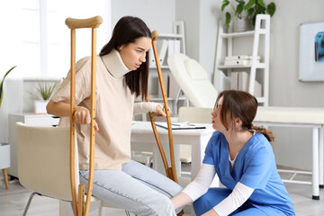 Wall Mural - Injured young woman with crutches after accident and doctor in clinic