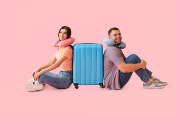 Canvas Print - Beautiful young happy couple of tourists with suitcase and travel pillows sitting on pink background