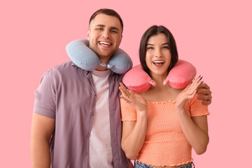 Wall Mural - Beautiful young happy couple of tourists with travel pillows on pink background