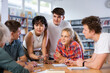 © JackF - Positive teenage students working and discussing in groups in college library