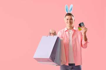 Wall Mural - Young man in bunny ears with shopping bags and credit cards on pink background. Easter Sale