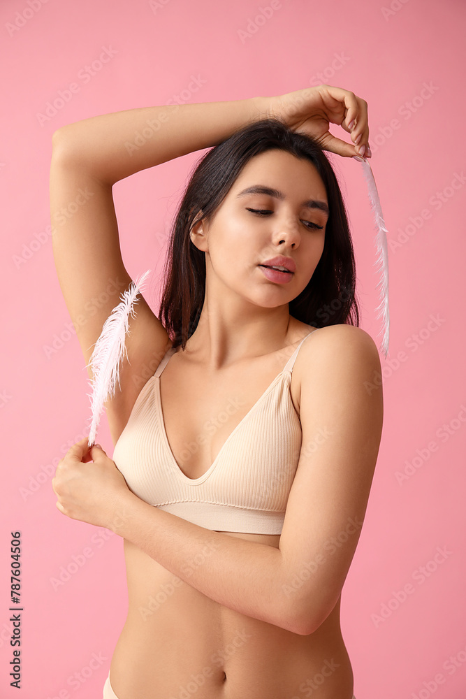 Pretty young woman with soft feathers on pink background. Epilation concept