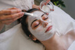 Woman getting facial care by beautician at spa salon. Face peeling mask, spa beauty treatment, skincare.