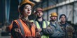 A group of construction workers, with a young woman at the forefront, pose in a confident manner against an industrial background