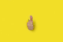 Hand With Thumb Up As A Sign Of Approval, Coming Out Of The Hole Of A Yellow Torn Paper Background.