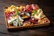 Plateau with different types of cheese and delicatessen meats, jamon, pastrami with dried fruits and sauces on dark boards background. Menu for a pub
